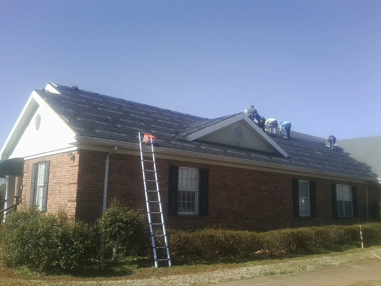 Crew tearing shingles off a brick ranch roof with a ladder set — Metal Roof Repair work by our crew in West Boylston