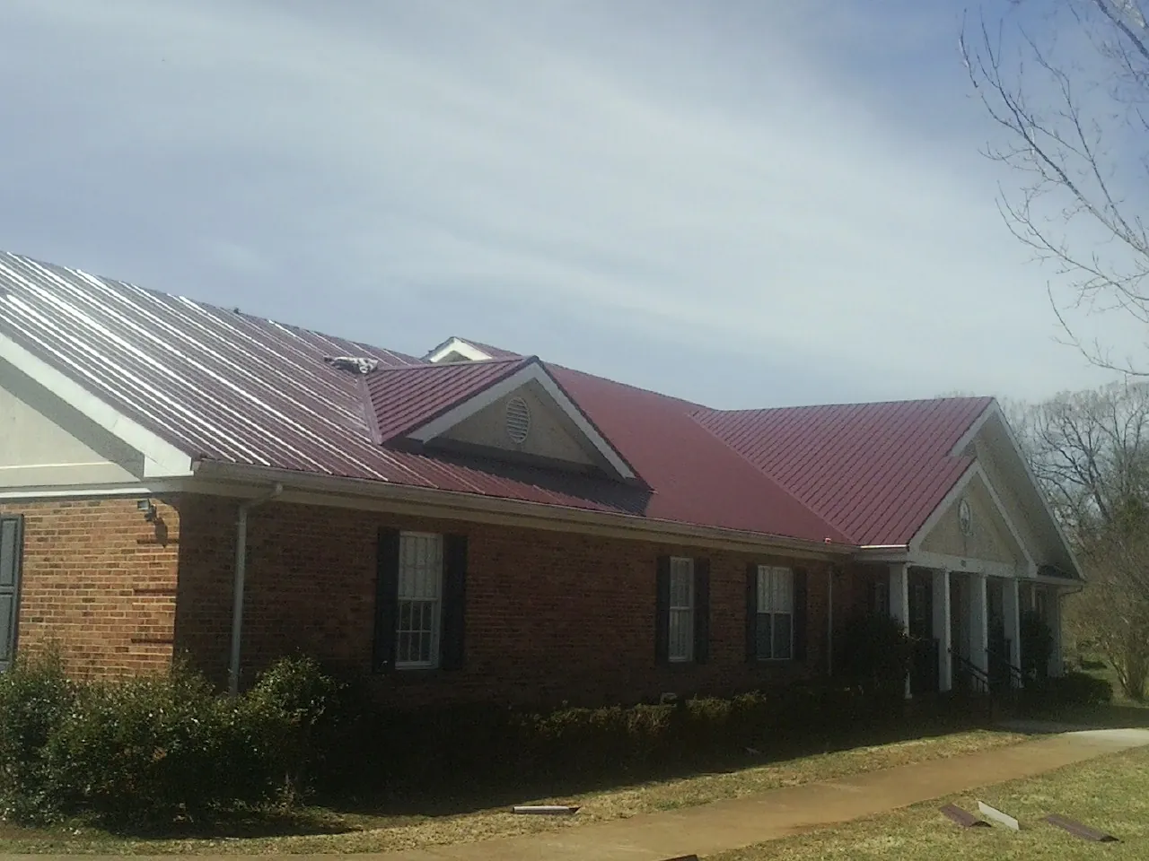 Red metal roof with gabled entries on a long brick building, from a Hail Damage Roof Repair job in West Boylston