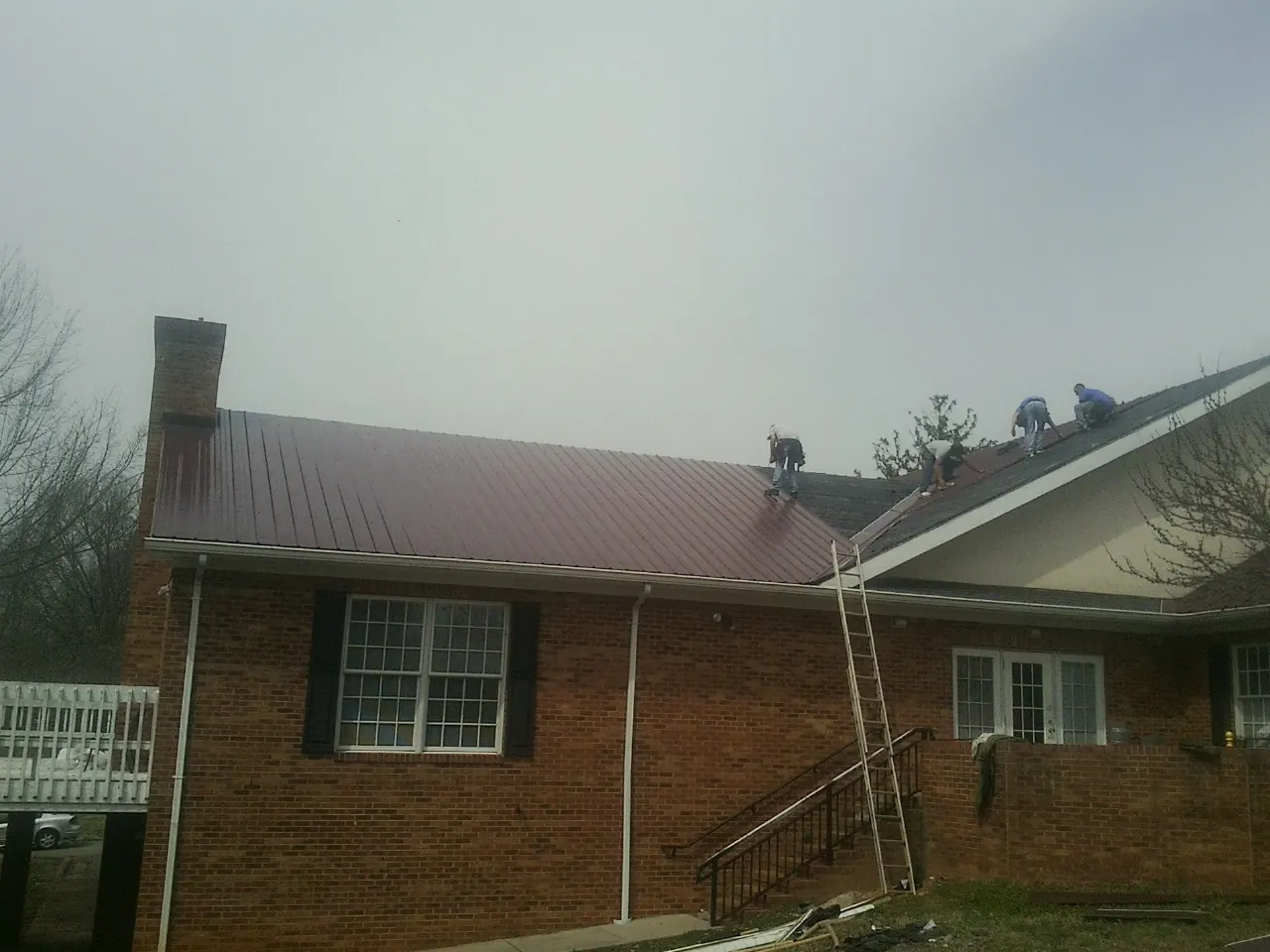 Crew setting red metal roofing panels on a brick home in West Boylston