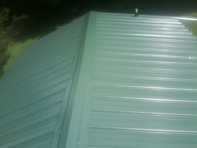 New green metal panels meeting at the ridge of a roof — Flat Roof Repair work by our crew in West Boylston