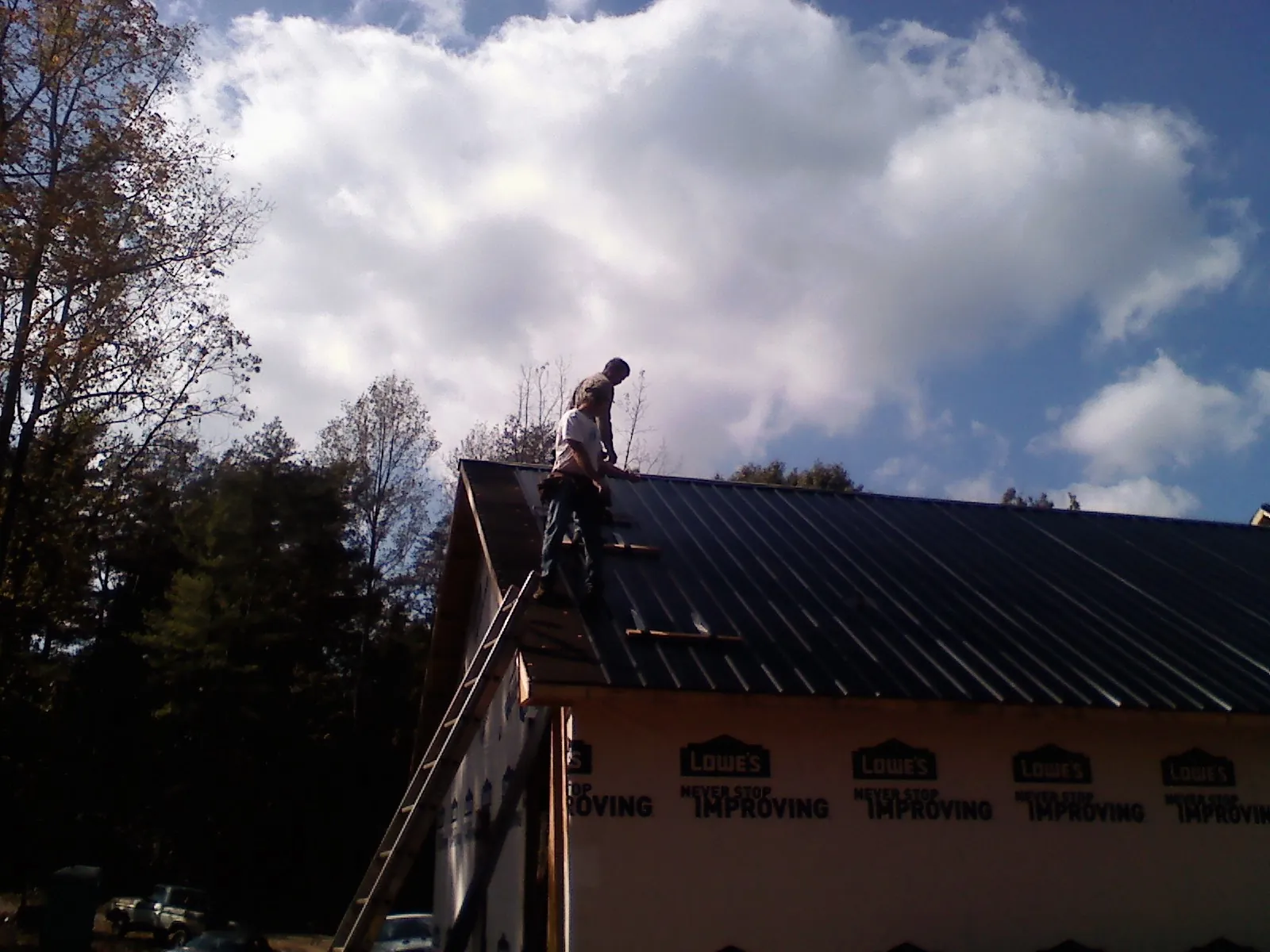 Roofer fastening dark metal panels high against a cloudy sky, from a Roof Inspection job in West Boylston
