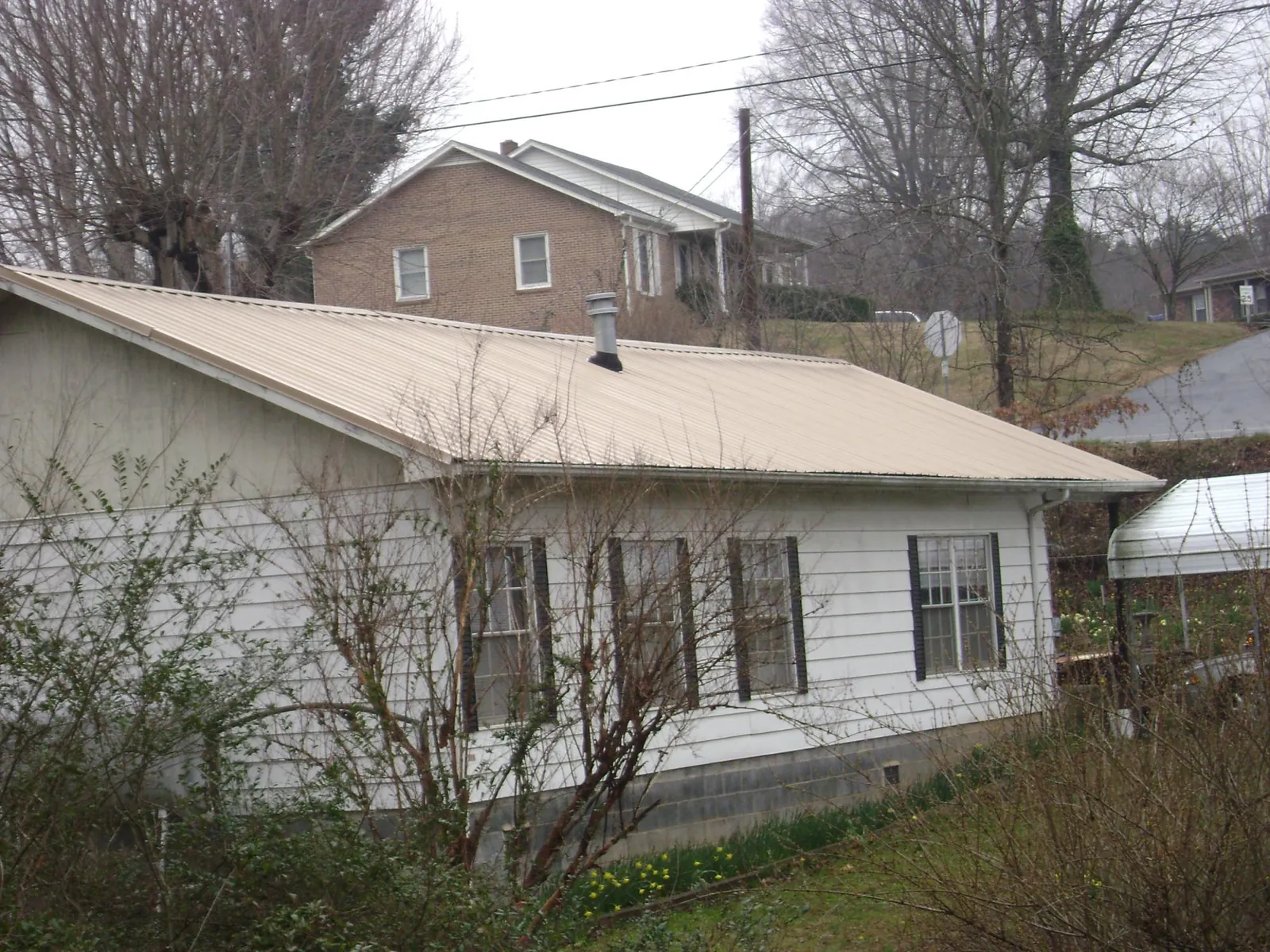 Tan metal roof on a white sided house set into a hillside — Commercial Roofing by Roofing Brothers in West Boylston